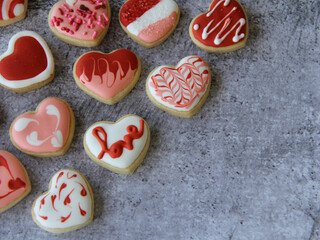 Heart shaped homemade cookies flat lay decorated with textured red and white icing designs for Valentine's Day on gray background with copy space, suitable for background, wallpaper or screensaver.