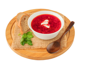 On a wooden cutting board in a bowl there is fresh borscht soup with bread, sour cream, and herbs.