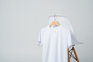 White blank t-shirt hanging on chair in empty room - obrazy, fototapety, plakaty
