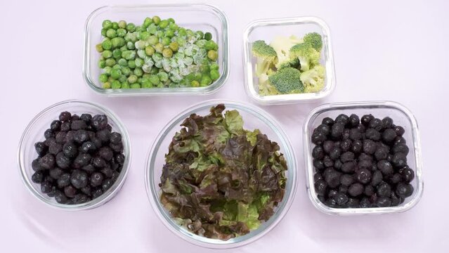 Green vegetables and berries in glass lunch boxes on pink background close-up, top view.