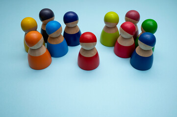 A red wooden peg doll surrounded by colorful wooden peg dolls, isolated on blue background. A leadership concept photo. A selective focus photo of the red peg doll.