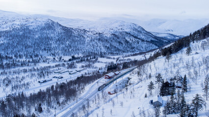 Aerial drone view of a norwegian passenger train standing on a platform at Mjolfjell station in the middle of epic countryside landscape. Winterscape, epic winter wiev.