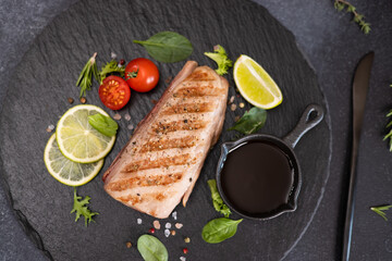 grilled cooked piece of tuna fillet on black stone serving board