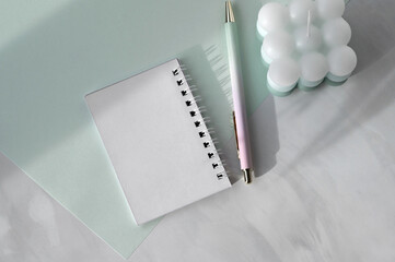 Soft elegant pastel green and white marble table background, open notebook with empty sheets mockup, pen and aesthetic candle, natural sunlight shadows