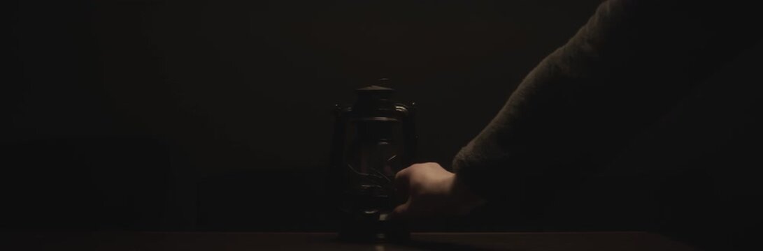 Anamorphic video of kerosene lamp light or an ancient lantern flickers in the dark. Old classic oil lantern burning with an orange flame. Male hand turn the lamp off.