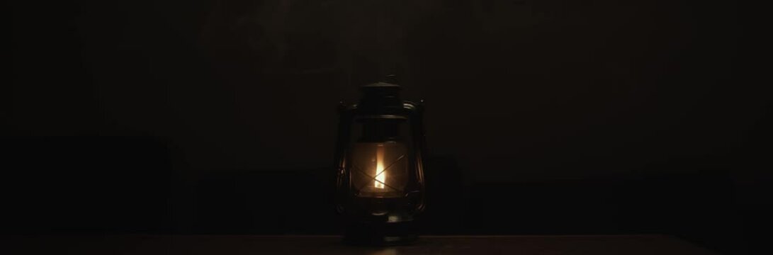 Anamorphic video of kerosene lamp light or an ancient lantern flickers in the dark. Old classic oil lantern burning with an orange flame. Male hand turn the lamp off.