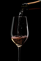 Wine pours into a glass from a bottle on a dark background splashes of wine
