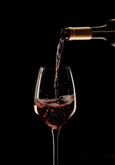 Wine pours into a glass from a bottle on a dark background splashes of wine