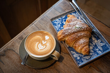Hot coffee latte with latte art milk foam in cup mug with Croissant on wood desk on top view. As...