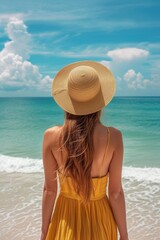 Fototapeta na wymiar Eine junge Frau mit einem Sonnenhut und einem gelben Sommerkleid am Strand 