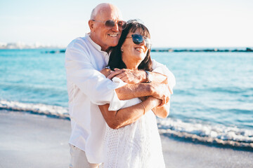 Happy bonding senior couple on the seashore at sunset enjoying vacation and retirement, two smiling...