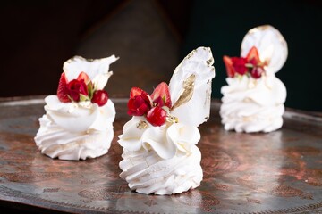 Obraz na płótnie Canvas Small size single serve Pavlova dessert cakes decorated with red berries and strawberries on serving plate in restaurant, dark background