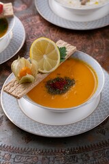 Creamy pumpkin or lentil soup in a bowl, served with lemon and dry herbs in white bowl, restaurant menu