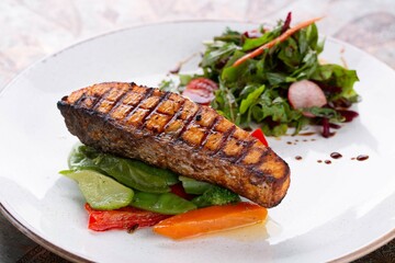 Grilled salmon steak with vegetables and herbs on white plate, restaurant menu