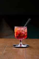 A glass of cold lemonade or fruit cocktail with straws in restaurant, dark background, relaxed evening drink with ice cubes.