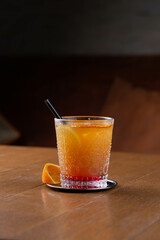 A glass of cold orange lemonade or fruit cocktail with straws in restaurant, dark background, relaxed evening drink with ice cubes.