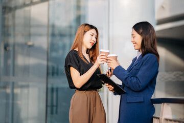 Businesswoman and woman going in city center in smart casual business style, talking, working together, stylish freelance people, holding coffee