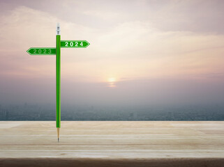 2024 and 2023 direction sign plate with green pencil on wooden table over city tower and skyscraper at sunset sky, vintage style, Business happy new year 2024 planning concept