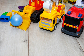 children's toy cars made of plastic, a fire truck, an excavator, a tractor, are on the floor.
