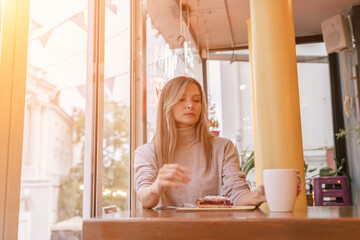Woman with blonde hair sips cappuccino in a cafe. She is holding the glass up to her face, taking a sip of the drink.