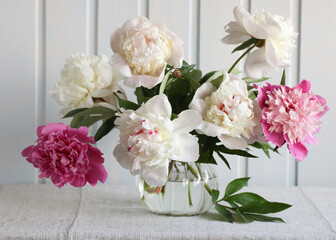 a bouquet of peonies in a jug on a table near a white board wall. garden flowers. summer concept, background.