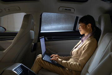 Businesswoman enjoying comfortable ride in luxurious limousine and working on laptop computer.