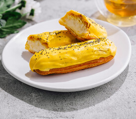 Fresh tasty eclair on white plate and cup of tea