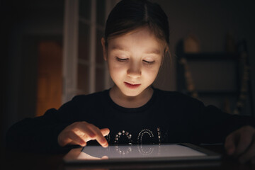 child looks at digital tablet in dark and touches screen with his finger
