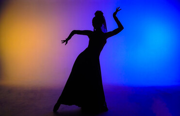 Fototapeta premium Woman dancer silhouette dancing on colorful background. Graceful dancer passionately dancing flamenco performing elements of Spanish style choreography.