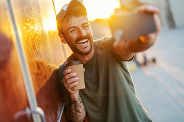 Portrait of a young man making selfies on a street with coffee to go.