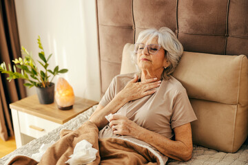 A sick senior woman with flu is lying in bed and having laryngitis.
