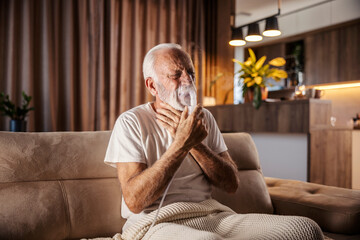 A senior man with throat ache is sitting at home and using nebulizer.