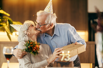 A senior couple is kissing and celebrating birthday at home.