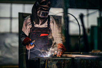 A heavy industry and metallurgy worker is welding metal parts in factory.