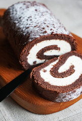 Chocolate sponge roll with vanilla cream on a wooden board on a light background