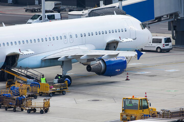 detailled close-up of an airplane on the ground at the terminal with luggage being unloaded