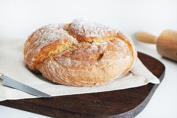 Fresh bread on a wooden board and linen tablecloth next to a knife on a white background