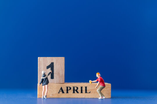 Miniature people painting a wooden block on April 1st