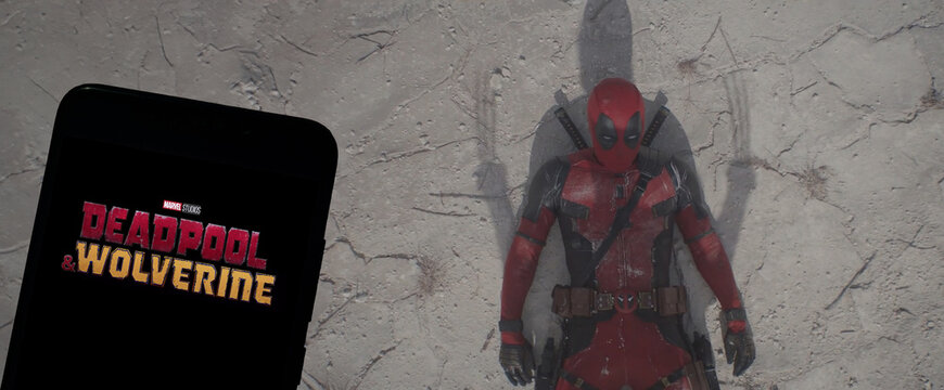 Logo of Deadpool & Wolverine movie on phone screen with movie trailer on the background on TV screen.