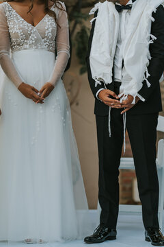 Pareja de novios de boda jud&iacute;a. El novio viste un talit blanco. imagen vertical.