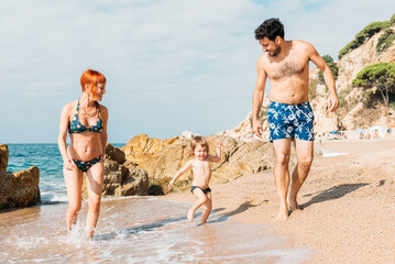 Happy couple walking on seashore with kid