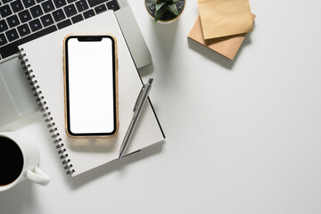 Smartphone with blank screen, notepad, coffee cup and laptop on white table