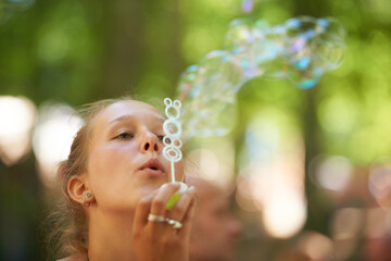 Woman, play and bubbles outdoors in blurred background, face and creative with freedom, happiness. Summer, game and gen z having fun in nature with peace in park and sunshine and water with soap
