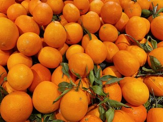 A fruit stand with a pile of oranges on it. There are green leaves at the bottom, and the oranges are round and smooth, looking very fresh.