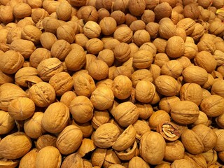 A pile of walnuts, one of which has been opened to reveal its interior. The walnuts are brown and...