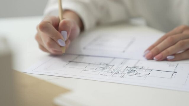 Closeup of professional young beautiful architect hand drawing blueprint while cooperative coworker measure house model by using ruler. Creative design and teamwork concept. Focus on hand. Immaculate.