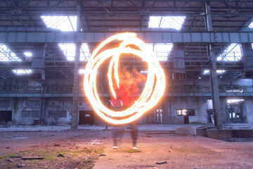 Fire dancer performing fire dance in long exposure in an old and abandoned industrial building