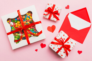 Red envelope with candy and gift box and Valentines hearts on colored background. Flat lay, top...