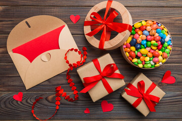 Red envelope with candy and gift box and Valentines hearts on colored background. Flat lay, top view. Romantic love letter for Holiday concept