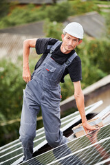 Portrait of man technician installing photovoltaic solar moduls on roof of house. Electrician in helmet building solar panel system outdoors. Concept of alternative and renewable energy.